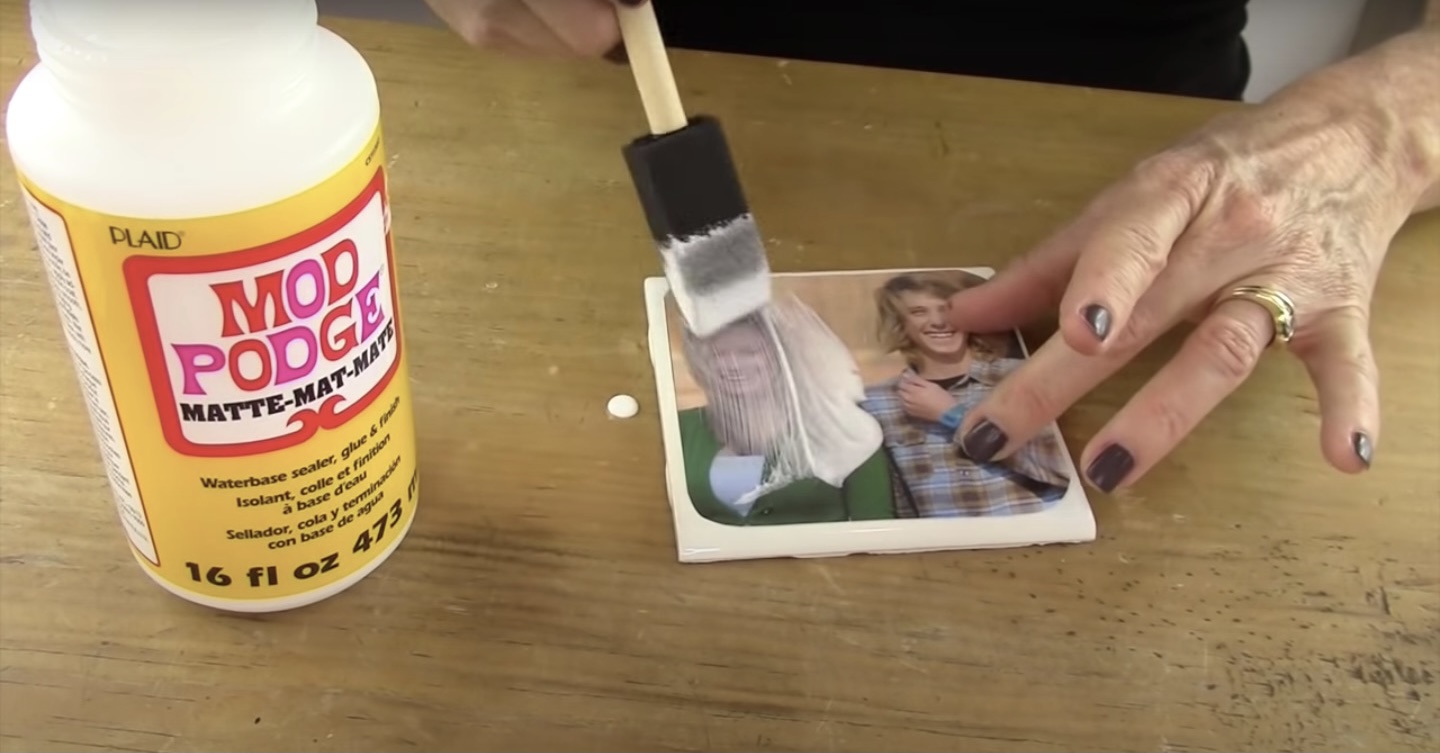 This photo shows how to seal the photos of loved ones to ceramic tiles with modpodge on the on the DIY Photo coaster project.